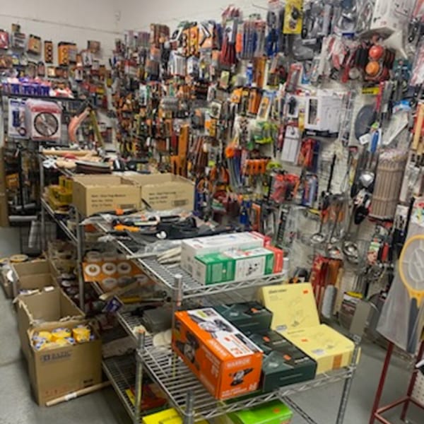 A cluttered variety store aisle with shelves and walls packed with hardware, tools, and household items.