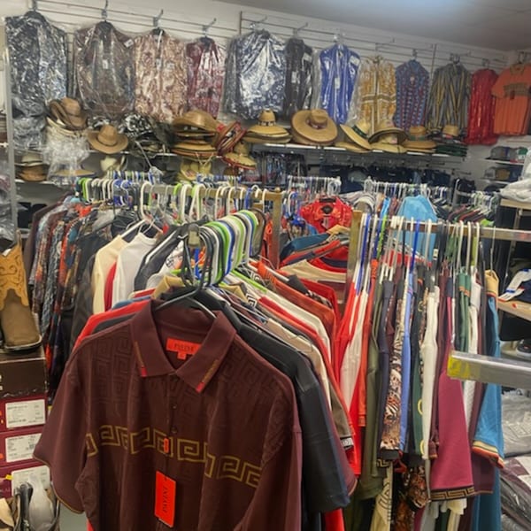 A variety store interior with racks of clothing, including shirts and cowboy hats, for sale.