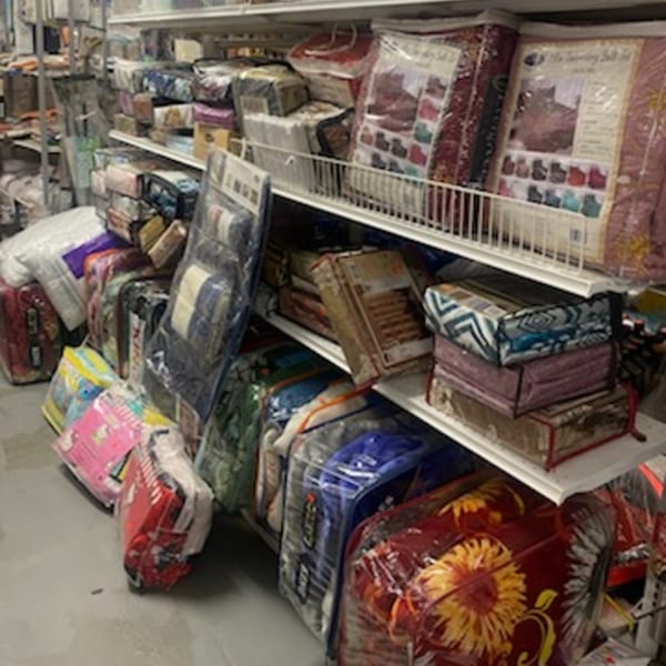 Shelves overflowing with packaged bedding and blankets in a variety store setting.