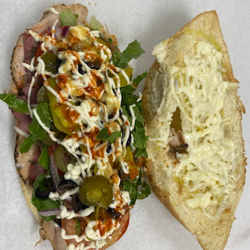 A large, open-faced sub sandwich with various toppings and sauces on a white surface.