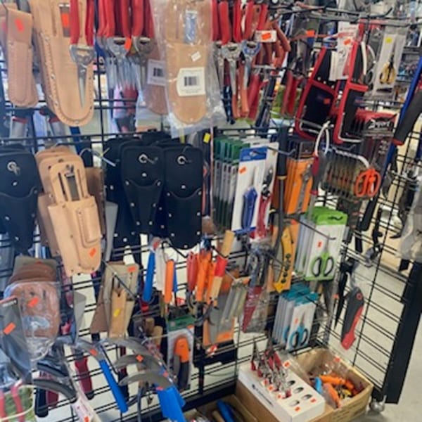 A retail display rack filled with various tools, including gardening shears, knives, and utility pouches.