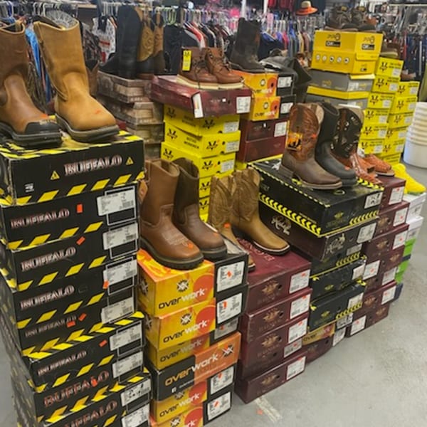 A retail display of various work boots and cowboy boots stacked on their boxes.