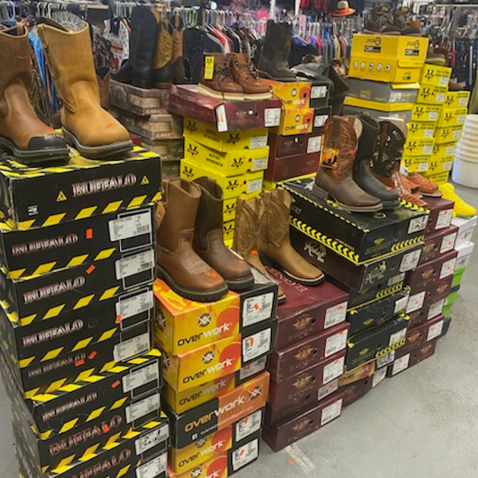 A retail display of various work boots and cowboy boots stacked on their boxes.