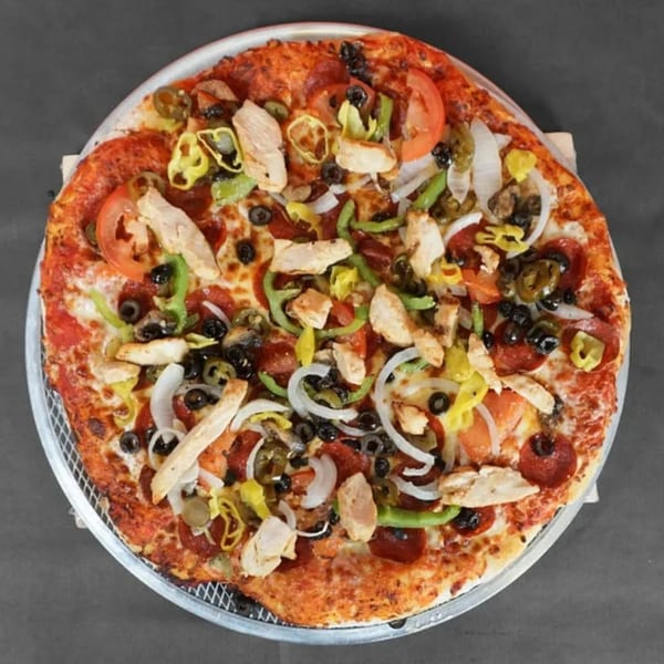A fully loaded pizza with pepperoni, chicken, olives, onions, and peppers on a metal tray.