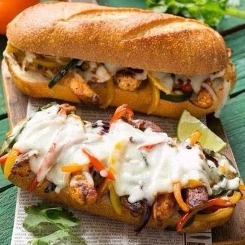 Two cheesy steak and pepper subs with a lime wedge on a wooden board.