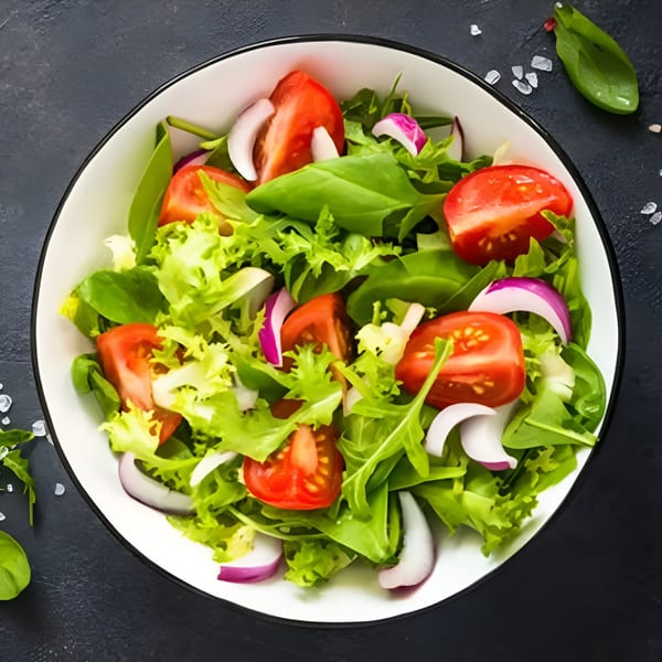 Fresh green salad with red tomatoes and purple onions in a white bowl on a dark background.