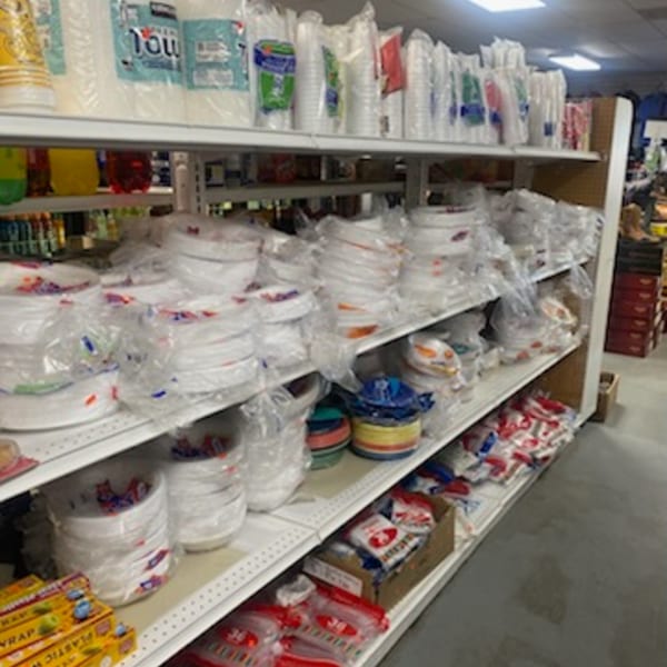 Shelves filled with various packaged disposable plates, cups, and plastic wrap at Planada Cafe & Variety.
