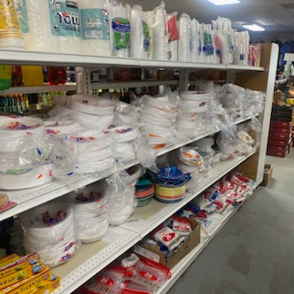 Shelves filled with various packaged disposable plates, cups, and plastic wrap at Planada Cafe & Variety.