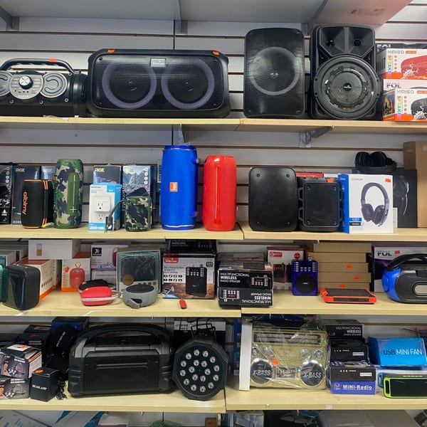 Shelves filled with various electronics, including speakers, headphones, and other gadgets, at Planada Cafe & Variety.