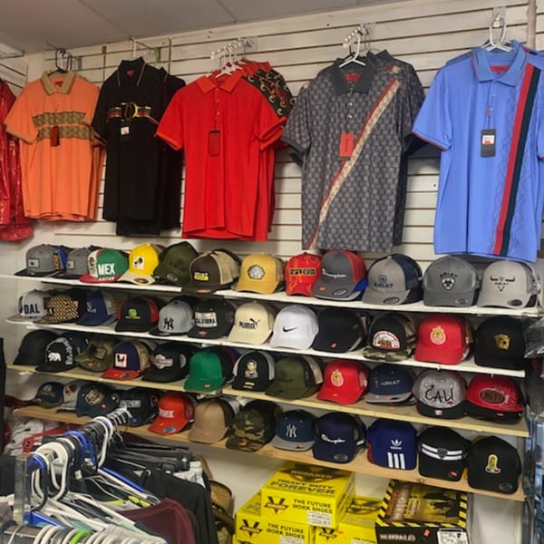 A variety store display with polo shirts hanging above shelves filled with baseball caps.