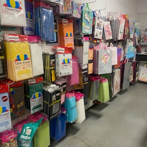 A variety of colorful party supplies, including table covers and gift bags, displayed on a wall.