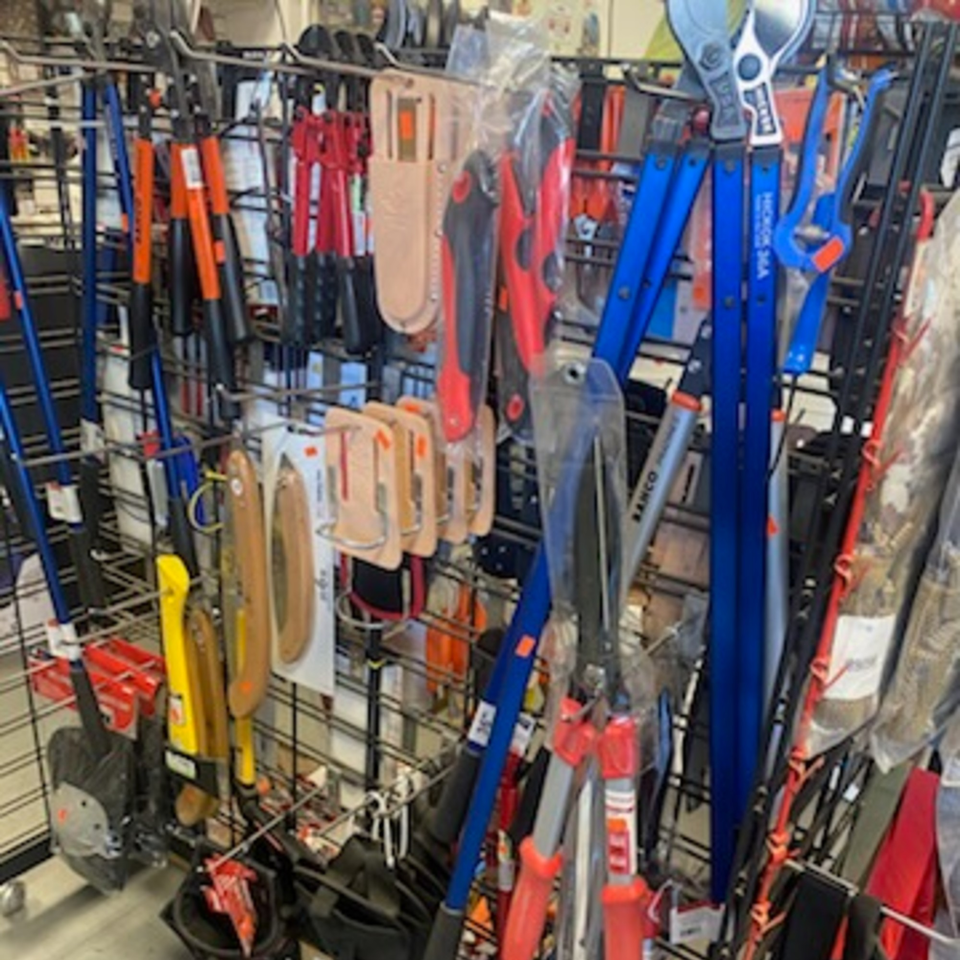 A retail display rack filled with various gardening tools, including blue and red pruners and shovels.
